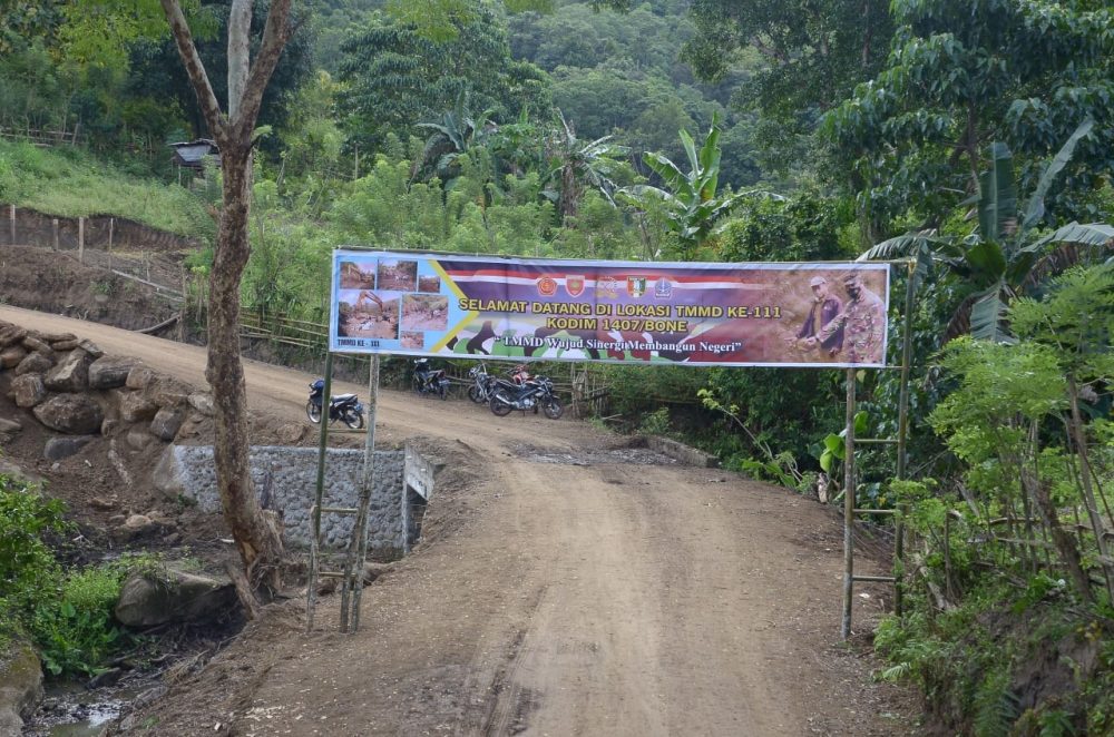 Papan Spanduk Selamat Datang Di Lokasi TMMD Ke-111 Suda Terbentang Di Atas Jalan Baru